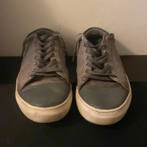 Säljer lanvins - Säljer ett par grå sneakers med vita sulor och mörkgrå snörning. Skorna har rund tå och platt sula, samt detaljer i mörkare grått vid tån och hälen. Perfekta för en avslappnad stil. Dom är i rätt bra skick