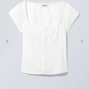 Vit topp  Weekday - Säljer en stilren vit topp från Weekday med fyrkantig ringning och korta ärmar. Toppen har en enkel och fräsch design, perfekt att matcha med jeans eller kjol. Tillverkad i mjukt bomullsmaterial.