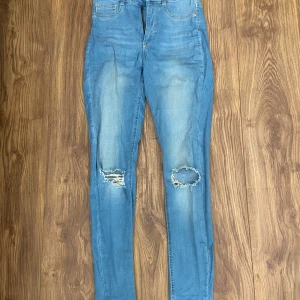 Blå skinny jeans med hål - Säljer ett par blå skinny jeans med slitna detaljer på båda knäna. Jeansen har normalhög midja. Skriv för fler bilder☺️