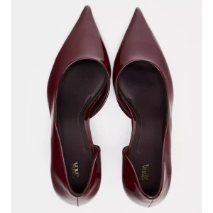 Vinröda pumps med spetsig tå från Zara - Snygga vinröda pumps från Zara i glansigt syntetmaterial. Skorna har spetsig tå och låg klack, vilket ger en elegant och modern look. Perfekta för dig som vill sticka ut med stilrena detaljer och en djup färgton.