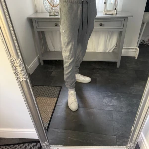 Grå Jordan mjukisbyxor med snörning - Snygga grå mjukisbyxor från Jordan med svart snörning i midjan och klassisk Jumpman-logga på benet. Byxorna har elastisk midja och muddar vid bensluten för en skön och avslappnad passform. Perfekta för chill eller träning.