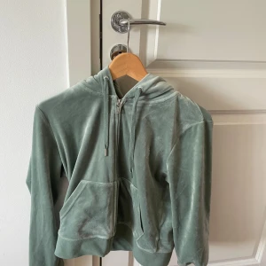 Grön velour hoodie Juicy Couture L - Mjuk och lyxig ljusgrön hoodie från Juicy Couture i velour. Tröjan har huva med snörning, dragkedja framtill och två stora fickor. Perfekt för en chill och trendig look.