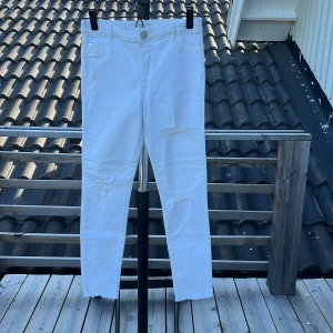 Vita jeans med slitningar River Island - Snygga vita jeans från River Island med slitna detaljer på benen och råa benslut. Klassisk femficksmodell med knapp och dragkedja. Perfekta för dig som gillar en fräsch och trendig look. Materialet är mjukt och stretchigt för extra komfort.