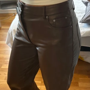 Bruna skinnbyxor från Pimkie - Snygga bruna byxor i skinnimitation från Pimkie med klassisk femficksdesign och raka ben. Byxorna har hög midja och stängs med dragkedja och knapp. Perfekta för dig som vill ha en edgy och trendig look.