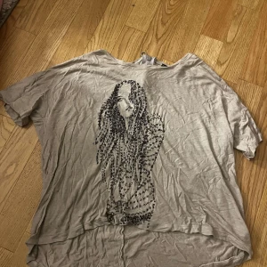 Beige topp med tryck och dragkedja - Cool beige topp med svart tryck av en tjej framtill, designad med bokstäver. Toppen har korta ärmar, rund hals och en snygg dragkedja med ringdetalj i nacken. 🩷