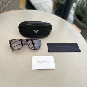 Svarta solglasögon Emporio Armani - Snygga solglasögon från Emporio Armani med mörktonade glas i nyskick. Kommer tillsammans med originalförpackning, putsduk och äkthetsintyg. Nypris 1600kr. Pris kan diskuteras!