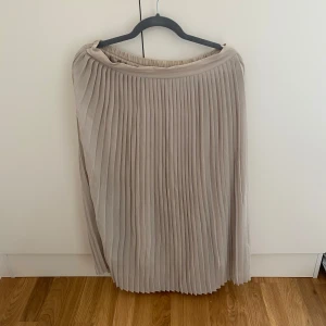 Plisserad beige långkjol - Snygg plisserad långkjol i beige med mjukt fall och elastisk midja. Perfekt för dig som gillar en stilren och trendig look. Kjolen har klassiska veck och passar till många olika outfits. Kan mötas upp i Trollhättan eller Alingsås. Kan skickas men då tillkommer en fraktkostnad.