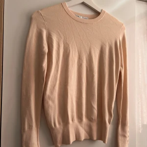 Beige Stickad Tröja Zara - Supersnygg beige stickad tröja från Zara med rund hals och långa ärmar. Ärmsluten har fyra stilrena guldknappar som ger en extra touch. Perfekt basic med en twist, passar till allt och är riktigt skön mot huden då den är mjuk! Aldrig använd! Nypris: 200-250kr