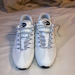 Nike Air Max 95 vita sneakers - Nike Air Max 95 i fräscht vitt med svarta detaljer. Skorna har en chunky sula med synliga Air Max-enheter, mesh och skinnpaneler samt coola snören med svartvitt mönster. Perfekta för dig som gillar streetstyle och vill sticka ut med klassiska sneakers.