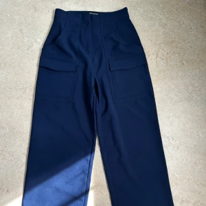 Mörkblå cargopants från PrettyLittleThing - Snygga mörkblå cargopants från PrettyLittleThing med raka ben och stora fickor framtill. Byxorna har hög midja och är tillverkade i ett mjukt bomullsmaterial. Perfekta för en chill och trendig look.