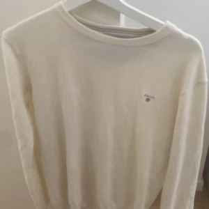 Vit stickad tröja från Gant - Klassisk vit stickad tröja från Gant med rund halsringning och diskret broderad logga på bröstet. Långärmad modell i mjukt material som passar perfekt till jeans eller chinos. Enkel och stilren design som funkar året runt.