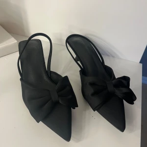 Svarta klackar med rosett och spetsig tå - Säljer ett par svarta klackar med rosett och spetsig tå, aldrig användna och i storlek 39