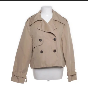 Beige kort trenchcoat med bälte - Kort trenchcoat, köpte på sellpy för 3 månader sen men bara inte använt den. Super fin, och jätte bra skick! Köpte för 400kr, säljer för 250💕