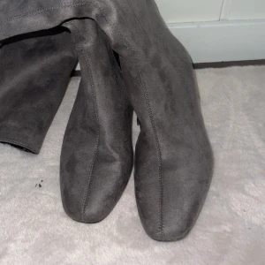 Grå mocka boots med klack - Snygga grå boots i mjuk mocka med låg klack och fyrkantig tå. Skorna har en stilren design och passar perfekt till höst- och vinterlooken. De är enkla att matcha och ger en trendig vibe till outfiten.