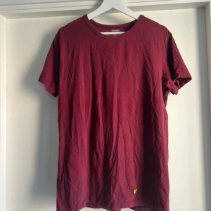 Vinröd t-shirt från Lyle & Scott - Vinröd t-shirt från Lyle & Scott med klassisk rund hals och korta ärmar. Tillverkad i mjuk bomull med lite stretch för extra komfort. På nedre delen sitter den ikoniska gula örn-loggan broderad. Perfekt basic med snygg passform.