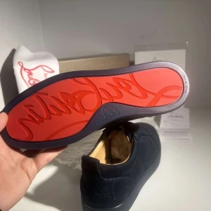Christian Louboutin Skor - Exklusiva mörkblå sneakers från Christian Louboutin i mjuk mocka med klassisk röd sula och ton-i-ton broderad logga på hälen. Skorna har rund tå, platt sula och snörning i matchande färg. Perfekt för dig som vill sticka ut med stilrena detaljer och lyxig känsla.