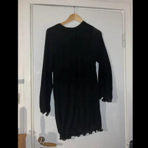 Svart volangklänning Gina Tricot - Svart kortklänning från Gina Tricot med långa ärmar och volangdetaljer vid ärmslut och nederkant. Aldrig använd, alltså väldigt bra skick!😊