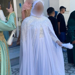 Vit klänning  - Elegant vit långklänning med glittrande paljetter över axlar och bröst, samt svepande cape-liknande tyg. Klänningen har långarmade armar och täcker hela kroppen. Perfekt för speciella tillfällen där du vill sticka ut med en lyxig passar flera storlek pga finns remmar för knytning passarflerastorlek.