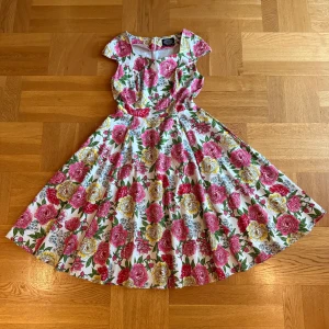 Blommig vit långklänning  - Superfin långklänning från H&R London med färgglatt blommönster i rosa, rött, gult och grönt på vit botten. Klänningen har korta ärmar, markerad midja och vidd i kjolen. Perfekt för sommarens alla tillfällen! Strl EU 38.