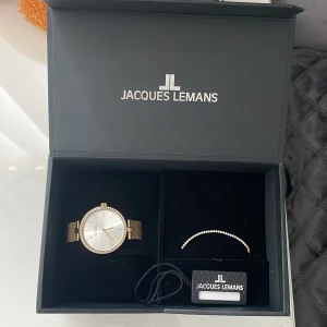 Guldig klocka från Jacques Lemans - Stilren klocka från Jacques Lemans med guldig mesh-länk och silverfärgad urtavla. Runt boetten sitter små stenar som ger extra bling. Klockan har minimalistisk design med tunna guldiga visare och index. Perfekt accessoar för att lyfta din outfit. Ordinariepris: 999kr