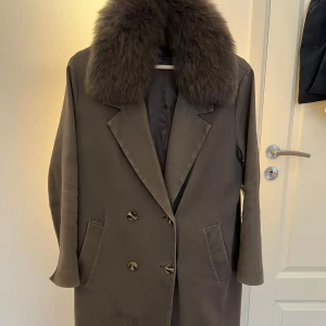 Meotine kappa med päls - Säljer en snygg brun kappa med dubbelknäppning och två fickor framtill. Jackan har en stor, fluffig pälskrage. Den har en fläck framtill som syns på bilden. Köpt för cirka 3500kr 