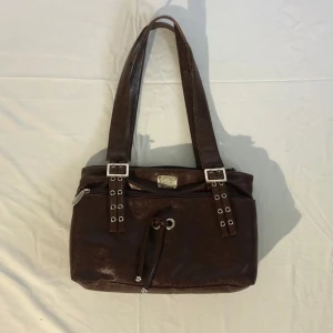 Axelremsväska dolce gabbana - En så klassisk väska från dolce & gabbana! I den perfekta bruna färgen med så många fina detaljer så som spänne och knytning. 