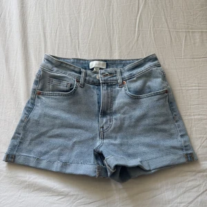 Ljusblå jeansshorts från H&M - Snygga ljusblå jeansshorts från H&M med klassisk femficksdesign och råa, fransiga benslut. Shortsen har mid midja och är tillverkade i mjukt denim. Perfekta för varma dagar och enkel att matcha med allt.