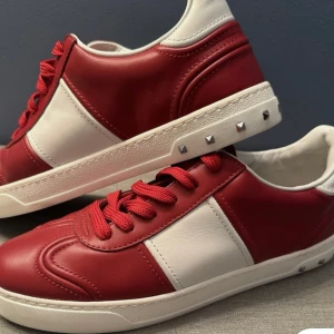 Valentino flycrews sneakers röd/vit - Snygga Valentino flycrews sneakers i rött och vitt skinn med röda snören och ikoniska nitar på sulan. Klassisk låg modell med rund tå och platt sula, perfekt för dig som vill sticka ut med stilrena detaljer.
