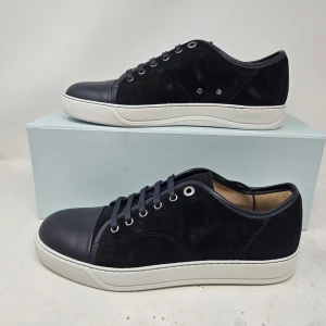 Svarta sneakers från Lanvin i mocka och skinn - Snygga svarta sneakers från Lanvin med ovandel i mocka och tåparti i slätt skinn. Skorna har vita platta sulor, rund tå och svarta snören. Perfekt för dig som gillar stilrena och lyxiga detaljer i din vardag.