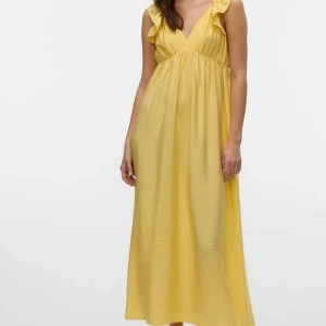 Gul långklänning med volang och knyt - Superfin gul långklänning med volangdetaljer på axlarna, v-ringning och öppen rygg med knytband. Klänningen har en luftig passform och är tillverkad i ett lätt, somrigt material. Perfekt för varma dagar när du vill känna dig extra söt och bekväm. Köpt för 549 använd en gång 