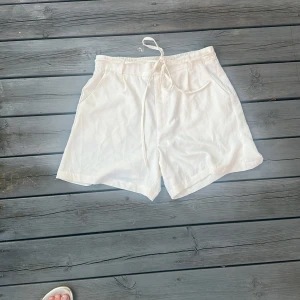 Vita shorts med snörning från Bik Bok - Snygga vita shorts från Bik Bok i storlek M. De har elastisk midja med snörning, fickor på sidorna och är tillverkade i 100% polyester. Perfekta för varma dagar när du vill ha en clean och fräsch look.