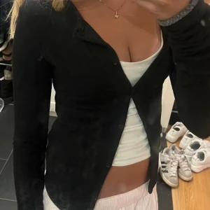 Svart kofta från Gina Tricot XS - Svart, figurnära kofta från Gina Tricot i storlek XS. Koftan har långa ärmar, knappar framtill och är tillverkad i mjuk bomullsmix. Perfekt att styla öppen eller stängd över ett linne eller topp.
