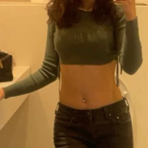 Grön croppad ribbad topp från Zara - Snygg grön croppad topp från Zara med långa ärmar och ribbad struktur. Toppen har trendiga snörningar i sidorna som gör att du kan justera passformen. Perfekt till jeans eller kjol för en cool look.