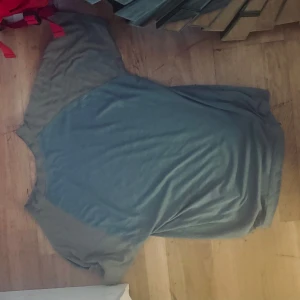 Grå/Blå t-shirt med KV på ärmen - Säljer en grå t-shirt med korta ärmar och initialerna 'KV' broderade på framsidan. Kriminalvården äldre modell .