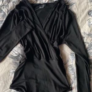 Svart omlott body - Snygg svart omlott body med långa ärmar och v-ringning. Tillverkad i ett mjukt och stretchigt material för en bekväm passform. Strl xs men som sagt stretchig så passar M. 