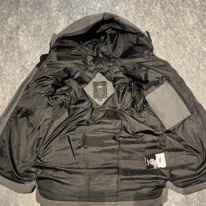 Grå dunjacka från Canada Goose - Säljer en stilren grå dunjacka från Canada Goose. Jackan har en pufferdesign med en praktisk huva och en broderad logotyp på ärmen. Perfekt för kalla dagar med sin långa ärm och dragkedja framtill. Passar både för stadsliv och naturäventyr. Pris går att  diskuteras