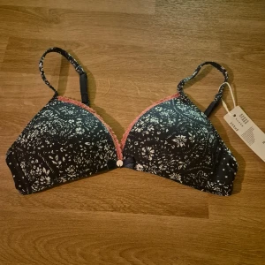 Ny bygellös BH från Esprit, 70AA  - Den är mörkblå med vita blommönster och rosa spetsdetaljer. Ovadderad. Helt ny med etiketten kvar. Kommer från ett konkurslager. Nypris 199, men kom med prisförslag. Kan skickas eller hämtas centralt i Malmö.