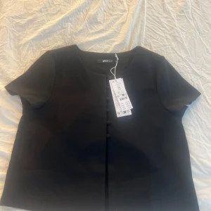 Svart kortärmad blus från Gina Tricot - Säljer en stilren svart blus från Gina Tricot med korta ärmar och knappar framtill. Perfekt för en elegant look. Blusen är i ett mjukt material som ger en bekväm passform. Aldrig använd, pris kan diskuteras💗