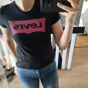 Svart t-shirt från Levi's - Säljer en svart t-shirt från Levi's med deras ikoniska logga i rött på bröstet. T-shirten har en normal passform och korta ärmar. Perfekt för en casual look.