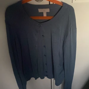 Blå kofta med knappar - Säljer en stilren blå kofta med knappar framtill. Perfekt för lager-på-lager och passar till många olika outfits. Den har långa ärmar och en rund halsringning.