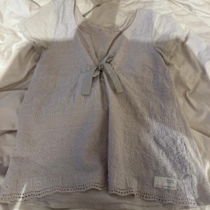 Vit topp från Odd Molly - Säljer en vit topp från Odd Molly med vackra broderade detaljer och knytband framtill. Toppen har korta ärmar och en fin spetskant längst ner. Perfekt för en stilren och bohemisk look.