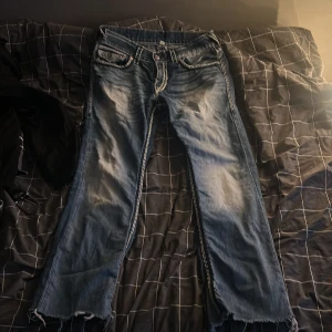 Blå jeans true religion  - Snygga blå jeans med unika broderade detaljer på bakfickorna. De har en klassisk femficksdesign och en slitningseffekt som ger en cool look. Perfekta för dig som vill ha något fett i garderoben!