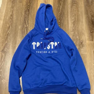 Blå Trapstar hoddie - Säljer en blå Trapstar hoddie. Den har en justerbar huva och ribbade muddar vid ärmslut och nederkant. Perfekt för en avslappnad stil.