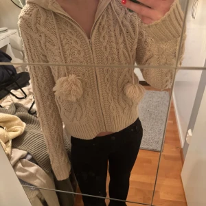 Beige stickad hoodie med dragkedja - Mysig beige stickad hoodie med dragkedja och stora tofsar på snörena. Superfin men kommer inte till användning längre 
