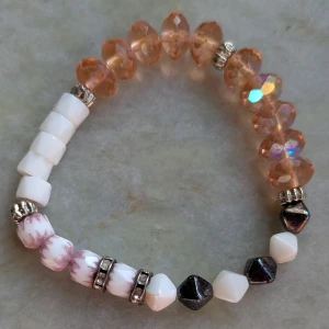 Färgglatt armband med pärlor - Unikt armband med en mix av vita, svarta och rosa pärlor samt glittrande orange kristaller. Armbandet har även små silverfärgade detaljer som ger en extra touch. Perfekt för att liva upp vilken outfit som helst!