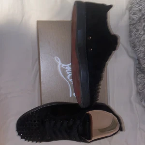 Christian Louboutin - Snygga svarta sneakers från Christian Louboutin med nitar på tån och den ikoniska röda sulan. Om du frågar mig så är skorna 9/10 skick men syns inte att det har används. Perfekt skor nu när värmen kommer. Man får även med allt som tillhör skorn så som box, dustbag, extra spikar, kvitto, och ett kort. Storleken är 43 men passar 44
