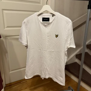 Vit t-shirt från Lyle Scott - Säljer en klassisk vit t-shirt från Lyle & Scott med en broderad gul logga på bröstet. T-shirten har en normal passform och är tillverkad i mjuk bomull. Perfekt för en avslappnad stil. Storlek: M Nypris 300kr