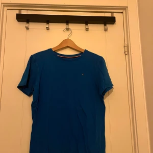 Blå t-shirt från Tommy Hilfiger - Säljer en snygg blå t-shirt från Tommy Hilfiger. Den har en liten logga på bröstet. Hör av dig vid funderingar!
