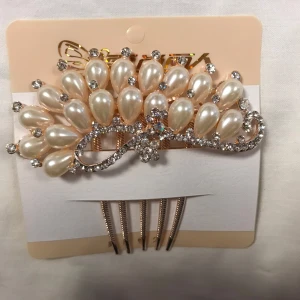 Hårkam med pärlor och strass - Elegant hårkam dekorerad med vita pärlor och glittrande strass. Perfekt för att ge en lyxig touch till din frisyr. Kammen har en vacker design som påminner om en blomma. 109kr/st , helt ny 