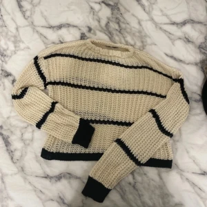 Beige stickad tröja med svarta ränder - Säljer en beige stickad tröja med svarta ränder. Tröjan har en rund hals och långa ärmar.